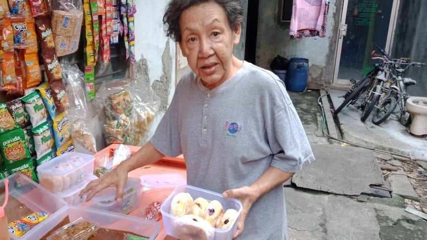 A trans woman with a box of cakes at a streetside vendor.