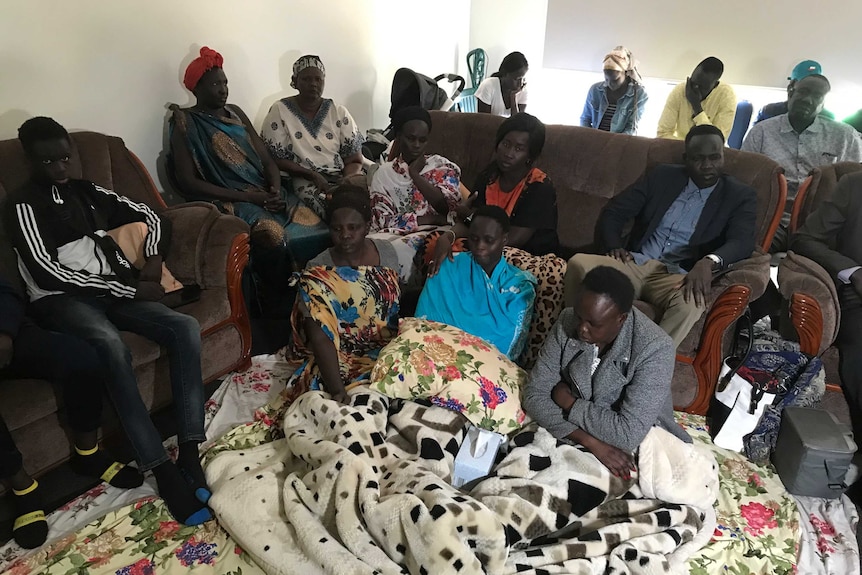 Aguer Akec's family sit on couches, chairs and on the floor mourning the death of Aguer.