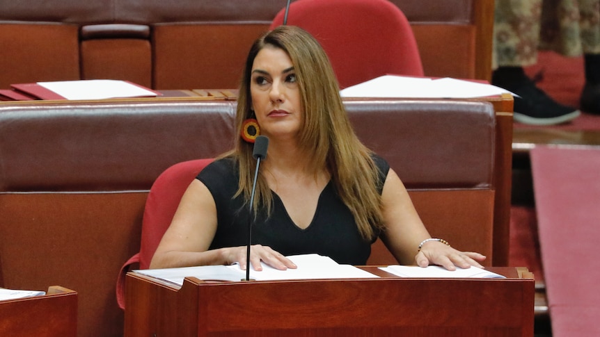 Lidia Thorpe, wearing earrings in the colours of the Aboriginal flag, sits in the senate, she looks up to the left