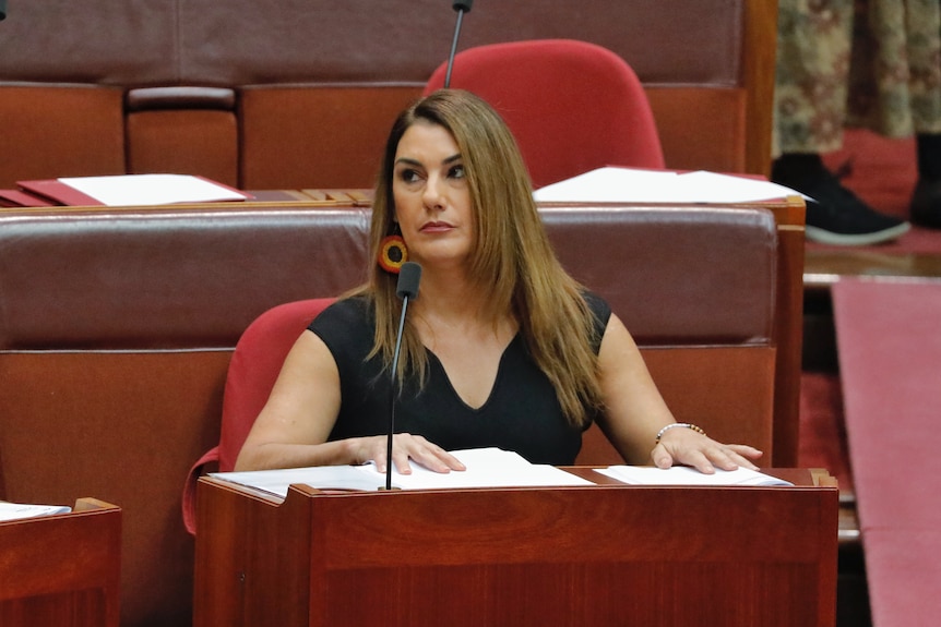 Lidia Thorpe, wearing earrings in the colours of the Aboriginal flag, sits in the senate, she looks up to the left