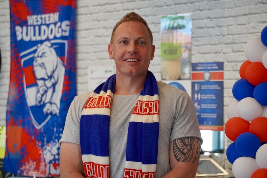 A man is pictured, smiling with a striped Western Bulldogs scarf