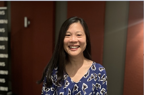 Christine is smiling with sun on her face. She has long dark hair and is wearing a blue top with a black and white pattern.