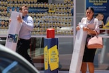 A man and two women clutching large cardboard boxes outside an Officeworks store.