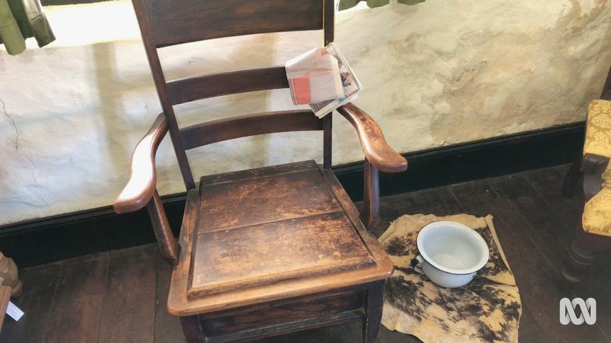 Chamber pot on floor beside wooden chair