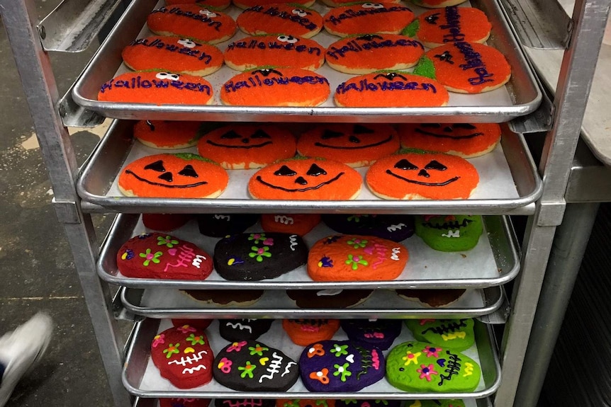 Freshly iced halloween cookies lay on trays outside of the oven