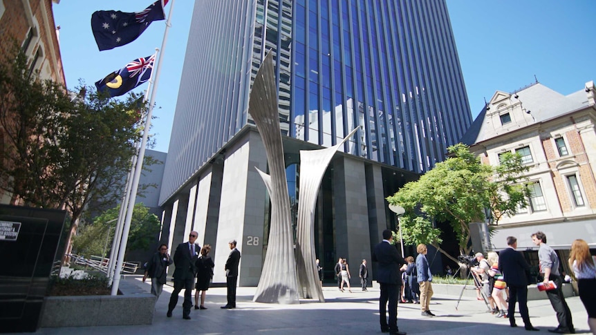 An exterior view from the ground of the high-rise David Malcolm Justice Centre, with a sculpture and people in the foreground.
