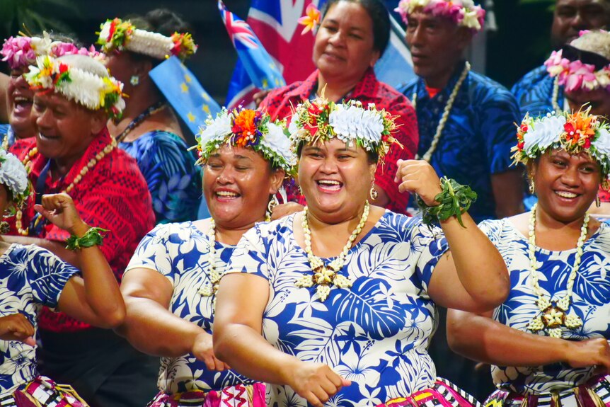 Women wearing colourful clothes and headdresses smile as they perform 