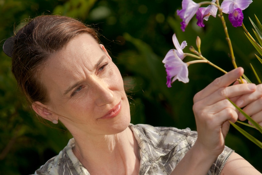 A woman looking at a purple flower she is holding.