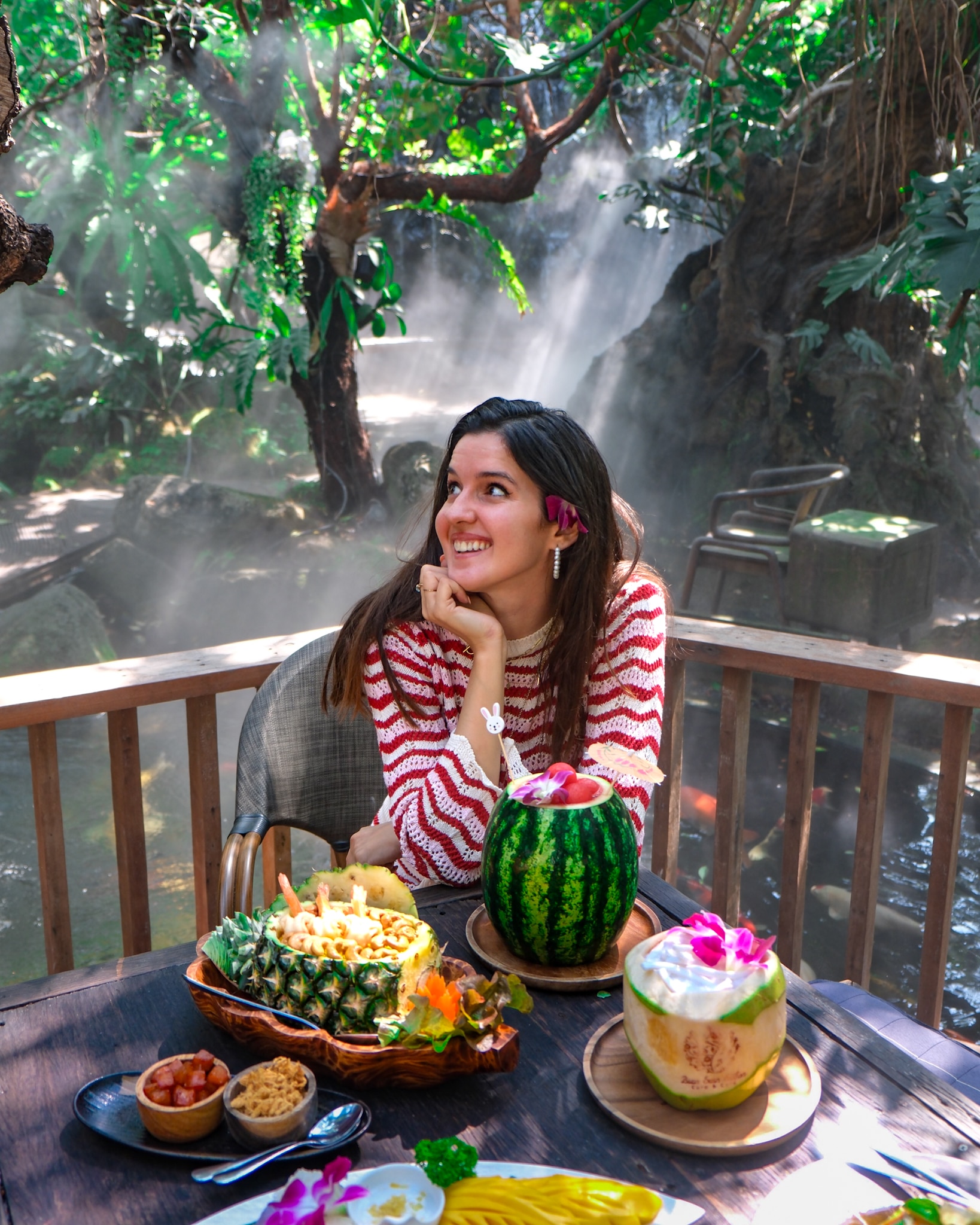 A woman sits smiling in front of a table full of food