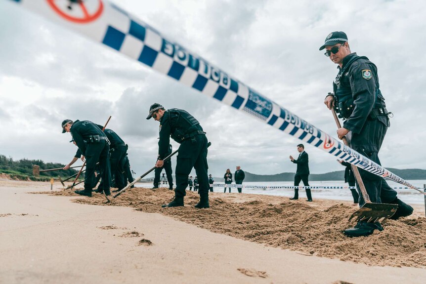 Police use a rake to sift through sand on Umina Beach