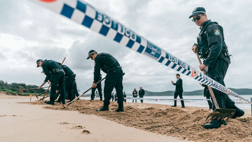 Police use a rake to sift through sand on Umina Beach