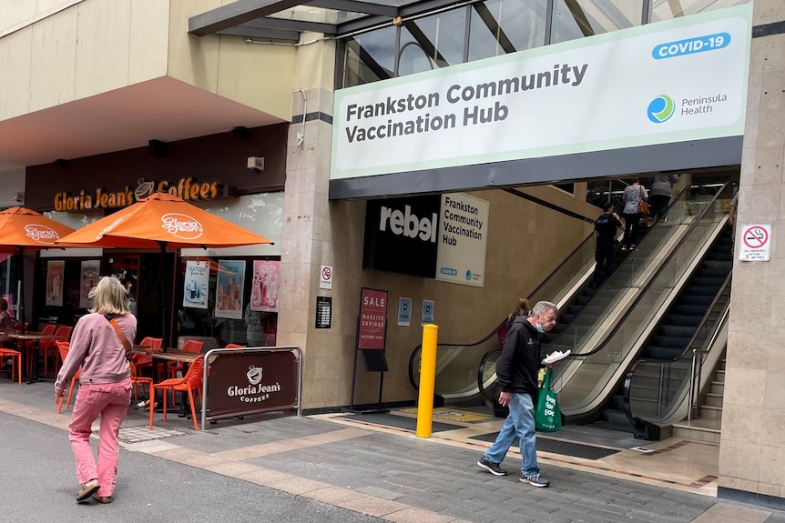 A board above an escalator says Frankston Community Vaccination Hub as a man and a woman pass by.