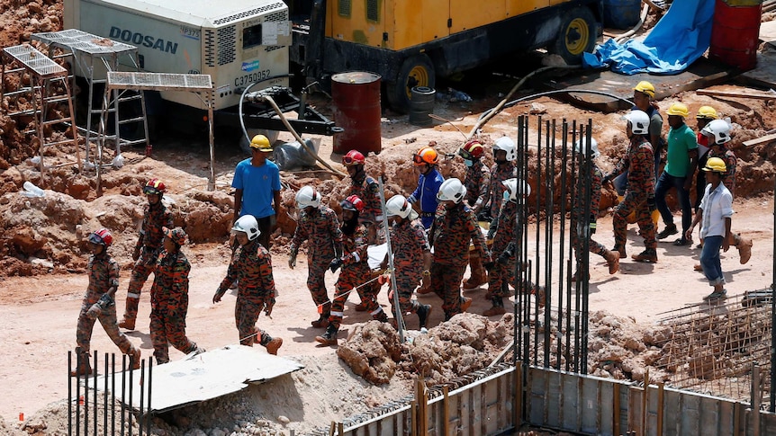 Rescue workers wearing hard hats are carrying a body on a stretcher at the construction site.