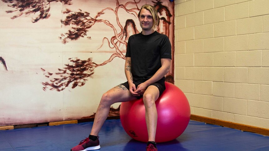 Deaf gym instructor Jarran Harris sitting on a fit ball