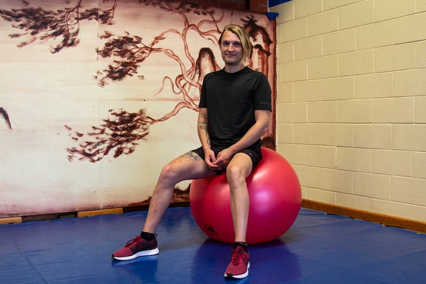 Deaf gym instructor Jarran Harris sitting on a fit ball