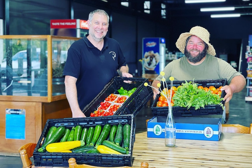 two men holding up boxes of fruit and vegetables