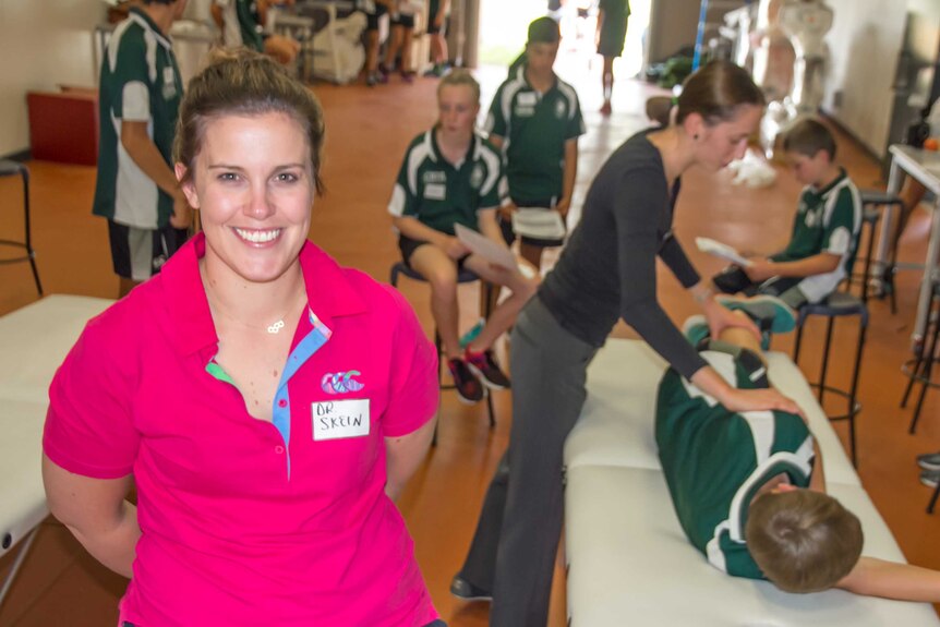 A woman in the foreground with a name tag Dr Skein in front of young people getting physiotherapy
