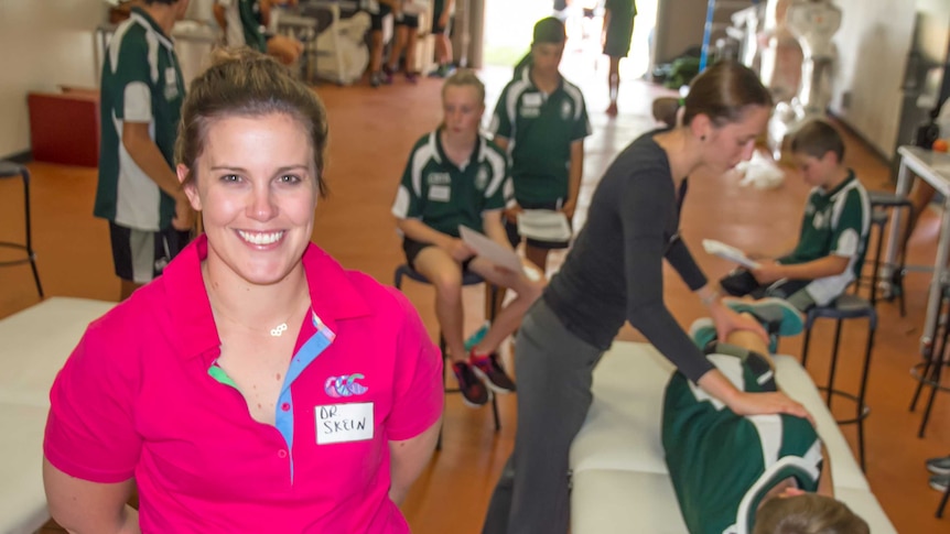 A woman in the foreground with a name tag Dr Skein in front of young people getting physiotherapy