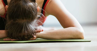 A woman rests her heads on her hands while laying on a light green, thin mat.