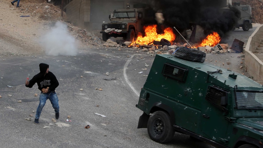 A Palestinian young man throws a bottle towards vehicles of Israeli security forces