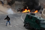 A Palestinian young man throws a bottle towards vehicles of Israeli security forces
