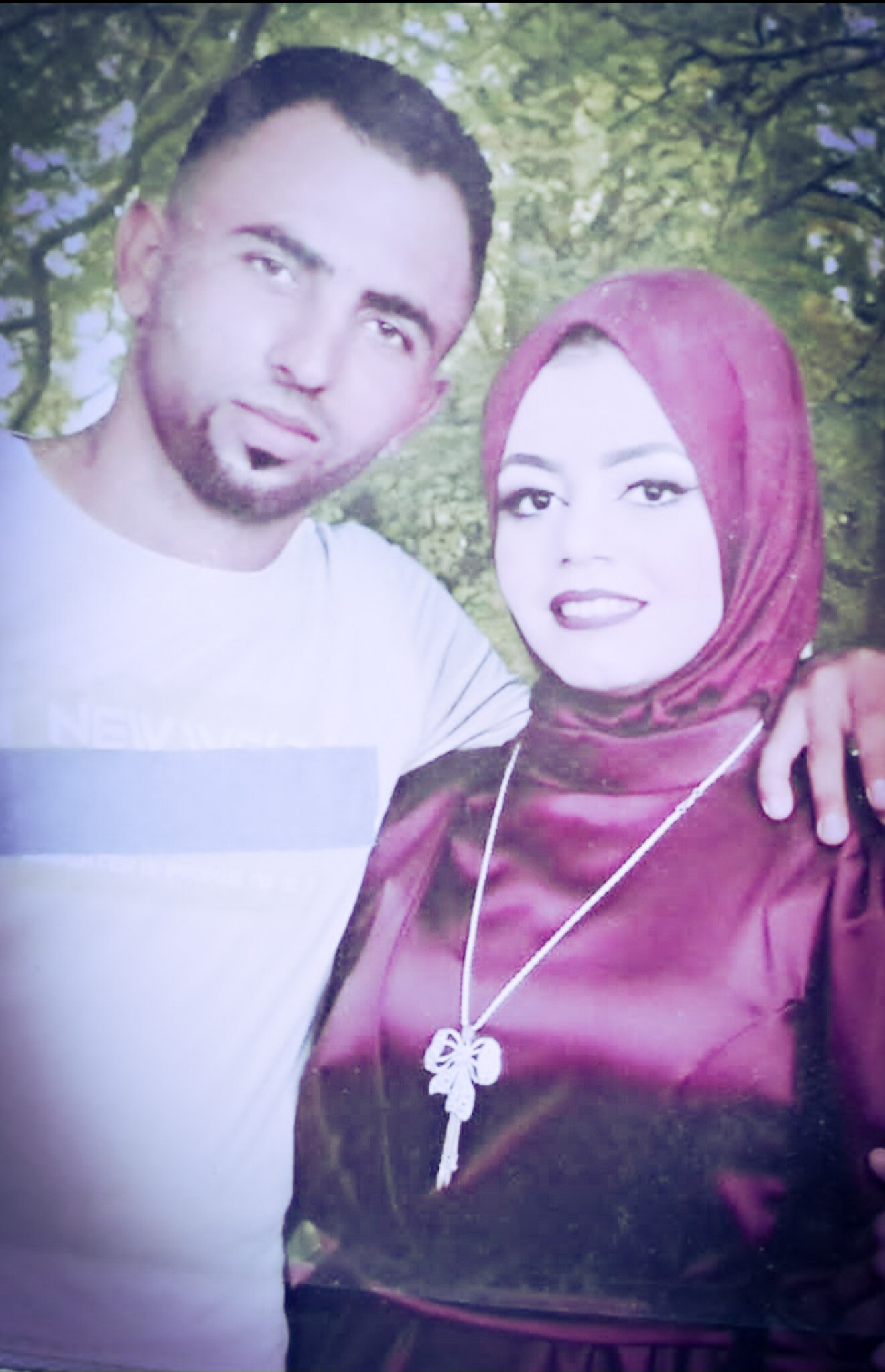 A man puts his arms around a smiling woman dressed in a pink hijab.