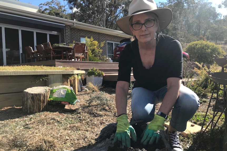 A woman in gardening gloves kneels beside a log she is filling with soil to plant flowers