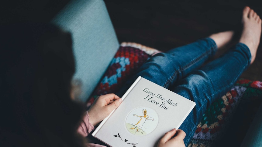 Girl sits on a couch reading children's book Guess How Much I Love You.