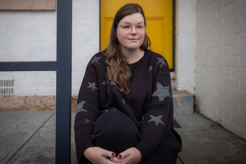 A young woman with glasses sits on a front step