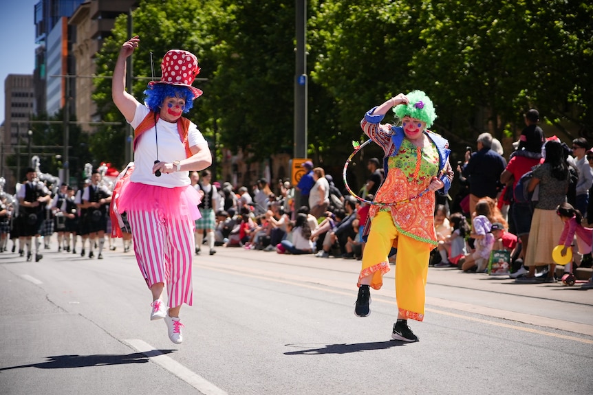 Two clowns dancing and skipping in a parade as people lined the streets