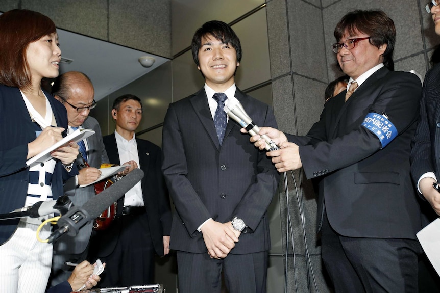 Kei Komuru clasps his hands in front of his torso while speaking to reporters in Japan