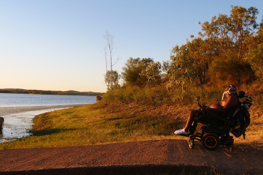 Man in wheelchair sits at lake watching sunset