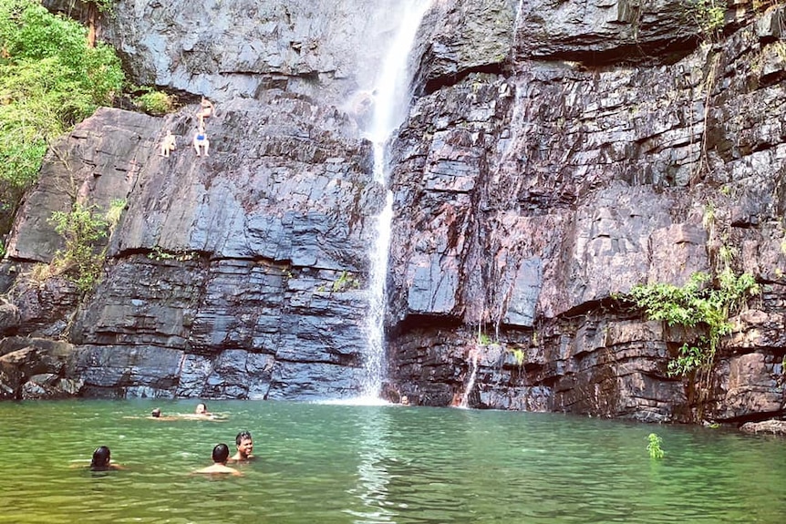 people swim in a clear waterfall pool