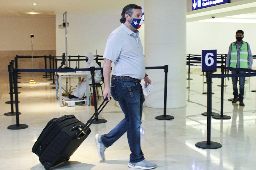 Ted Cruz in a Texas flag wheeling a suitcase through an airport