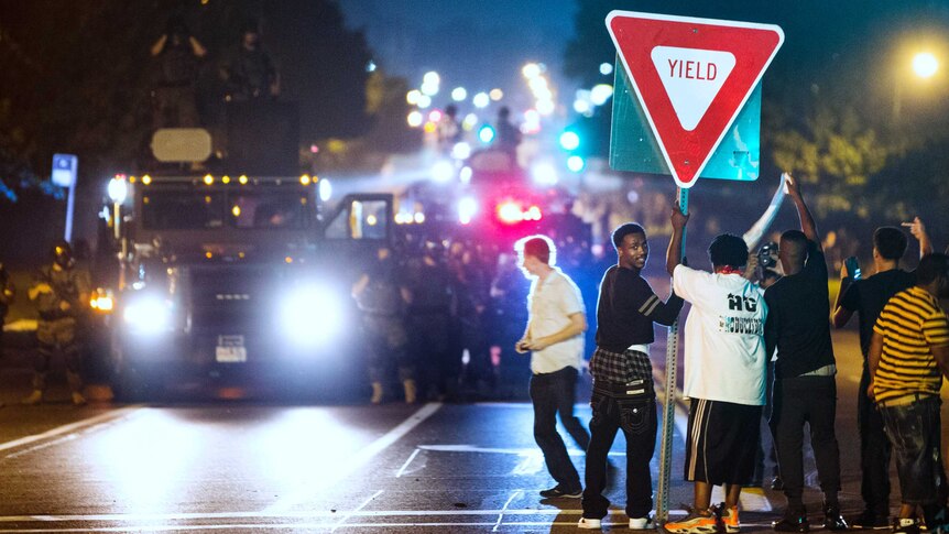 Members of a rowdy group of demonstrators stand with a road sign in Ferguson