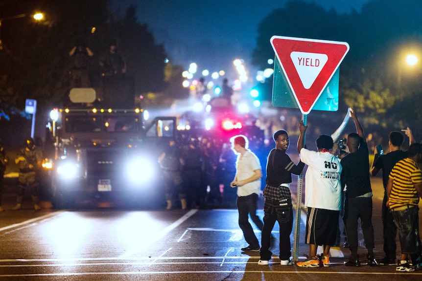 Members of a rowdy group of demonstrators stand with a road sign in Ferguson