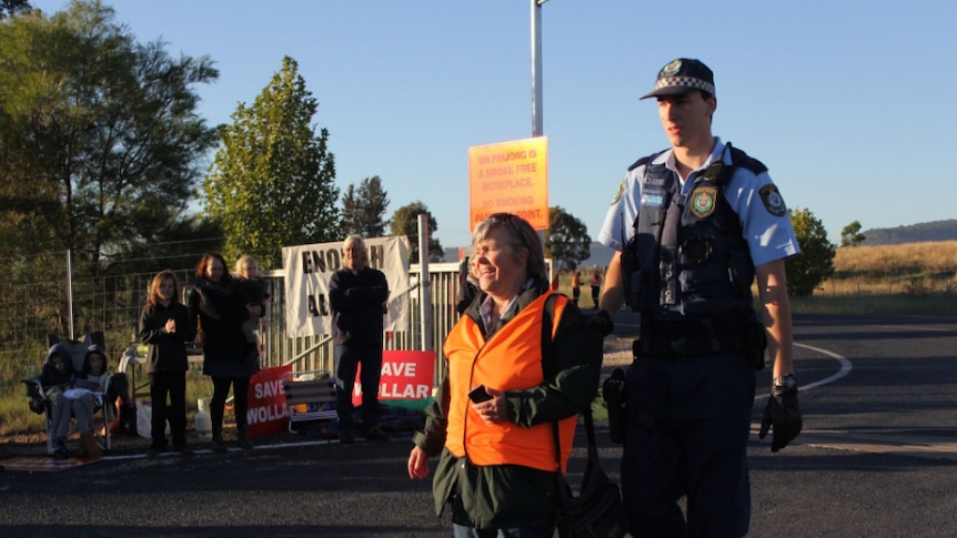 Woman in orange high visibility vest led away by police on country road