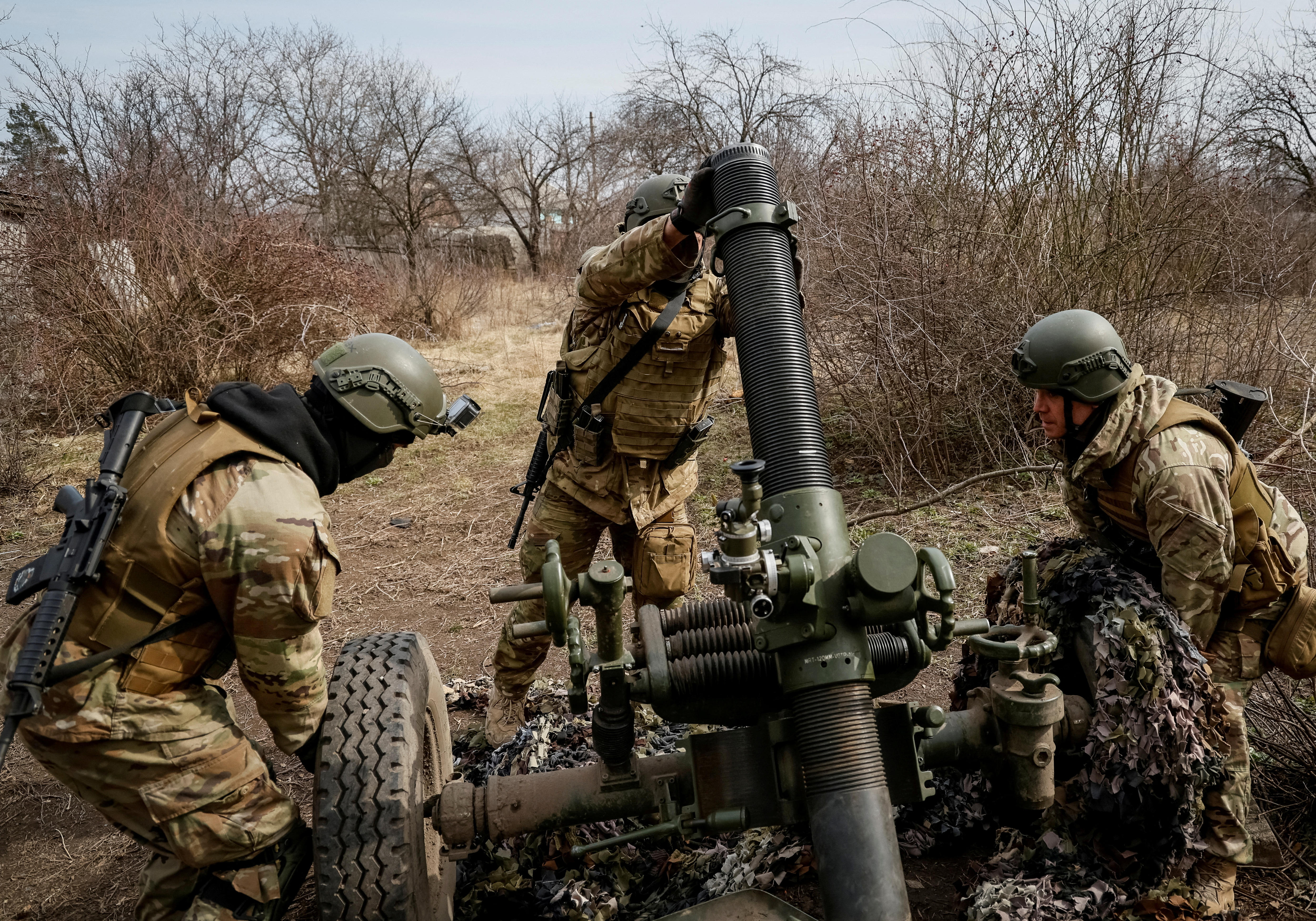 Three soldiers operate a missile launcher in light scrub