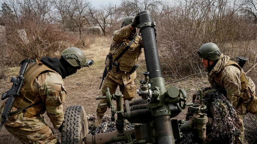 Three soldiers operate a missile launcher in light scrub