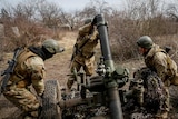 Three soldiers operate a missile launcher in light scrub