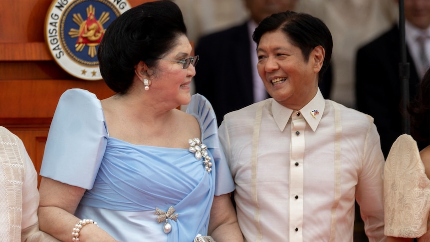 An elderly Filipina woman and a younger Filipino man in formal attire, both smiling