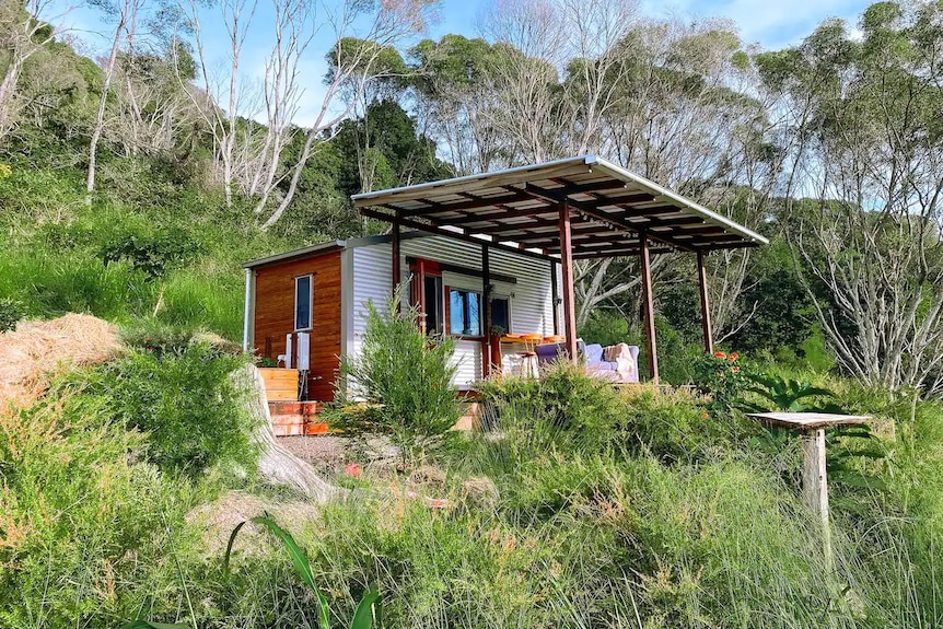 A tiny house with a big covered deck on a hill.