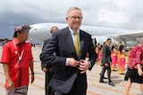 Anthony Albanese in front of an airplane with several people in bright red and yellow in the background