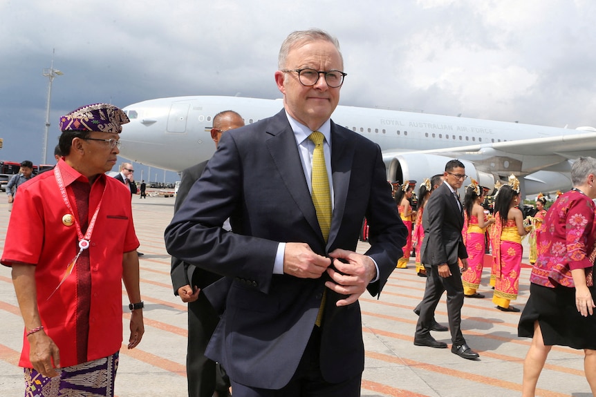 Anthony Albanese in front of an airplane with several people in bright red and yellow in the background