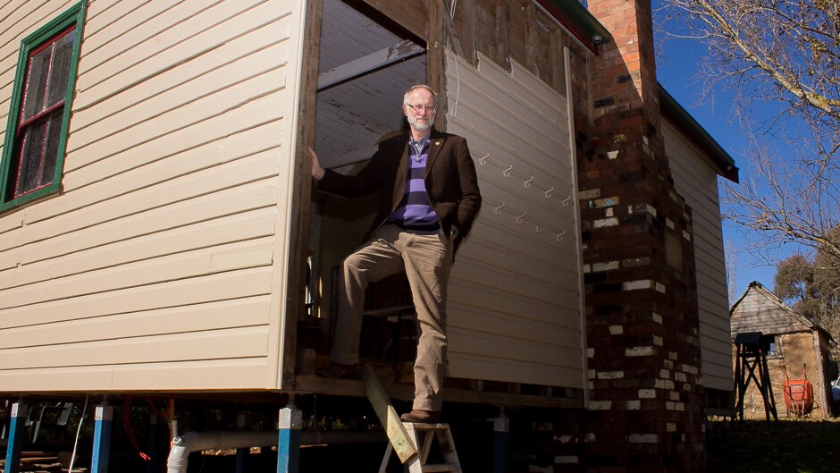A man standing on the steps of a small country school house that's being restored