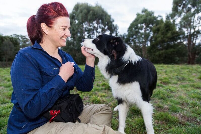 Trainer Tracy Edwards smiling as she holds the mouth of a conservation detection dog in parkland