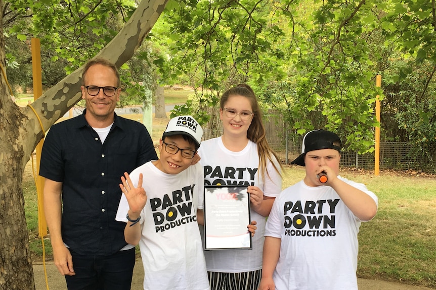 Luke stands smiling outside with some children who are wearing 'party down' t-shirts.