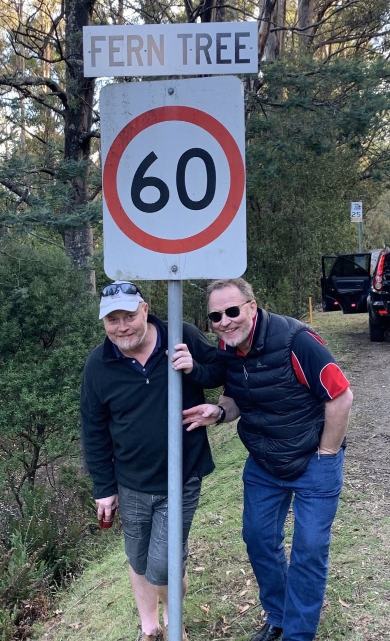 Two identical twin brothers pose for a photo under a road speed sign.