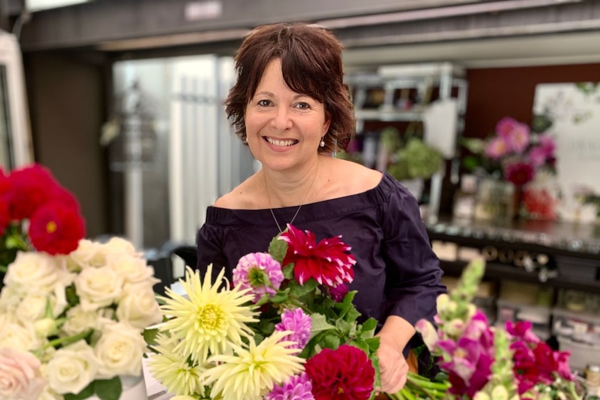 A woman smiles at the camera, surrounded by bouquets of flowers.