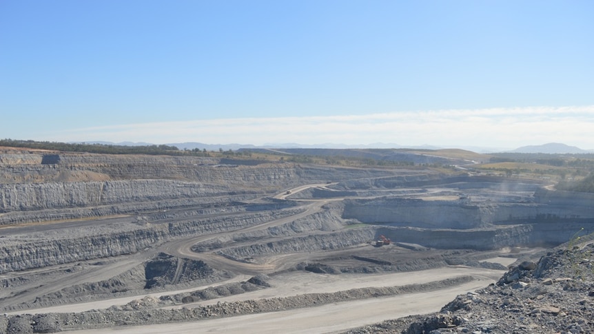 An open cut coal mine with high grey walls surrounded by farmland